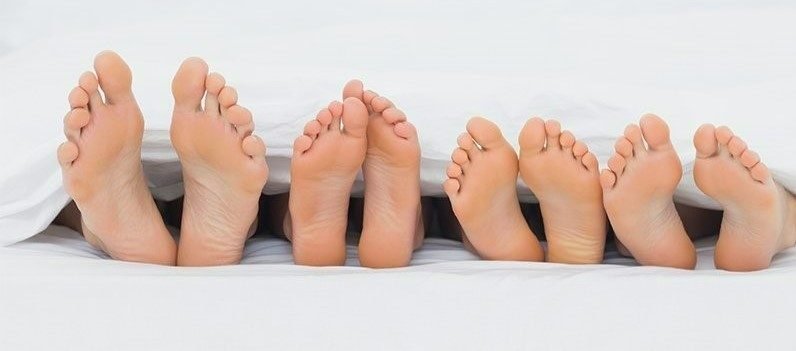 Four pairs of bare feet resting at the end of a bed